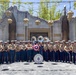 A U.S. Marine Corps band from Camp Pendleton, California poses for a group photo in front of an ornate themed structure, likely at a Disney theme park (Avengers Campus area). The group includes approximately 25-30 uniformed Marines holding various instruments, flanked by two costumed characters including Captain America. A large bass drum in the foreground bears the inscription referencing the 1st Marine Division Band, Camp Pendleton, CA.