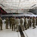 A large group of military personnel in camouflage uniforms are gathered in an aircraft hangar around an F-16 Fighting Falcon jet. The aircraft bears the markings of the 177th Fighter Wing (177 FW) from New Jersey Air National Guard, nicknamed 'The Jersey Devils,' with tail code AC and serial number AF 87-225. A briefing or orientation appears to be taking place in front of the aircraft.