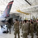 A group of military personnel in camouflage uniforms are gathered inside an aircraft hangar for what appears to be a briefing or demonstration around an F-16 Fighting Falcon jet. The aircraft's tail markings clearly identify it as belonging to the 177th Fighter Wing (177 FW) of the New Jersey Air National Guard, with tail code 'AC' and number 225. One individual in a flight suit appears to be conducting a hands-on demonstration or inspection of the aircraft's underside.