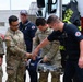 U.S. Army soldiers in OCP camouflage uniforms are receiving a demonstration of a Hurst rescue tool (commonly known as the 'Jaws of Life') from firefighters near a fire truck. The setting appears to be at the 177th Fighter Wing base in Atlantic City, NJ, suggesting an inter-service training or familiarization exercise. A civilian firefighter wearing a name tag reading 'Torres' is showing the equipment to the military personnel.