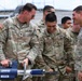 A group of U.S. Army soldiers in OCP (Operational Camouflage Pattern) uniforms are gathered together, laughing and smiling while examining a Hurst Jaws of Life hydraulic rescue tool. The mood is lighthearted and informal, suggesting a training demonstration or familiarization exercise. Name tapes visible include 'KNIGHT,' 'LEON,' and 'FRANCISCO,' all bearing U.S. ARMY identification.