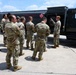 A group of military personnel in camouflage uniforms are gathered around a large fuel tanker truck on what appears to be a military installation or airfield. One soldier appears to be conducting a briefing or demonstration, pointing at the truck's equipment panel. The tanker displays hazmat placard number 1863, indicating aviation fuel.