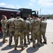 A group of military personnel in OCP (Operational Camouflage Pattern) uniforms are gathered around a fuel tanker truck for what appears to be a training or briefing session. One soldier facing the group appears to be instructing or addressing the others near the tanker. The setting is an outdoor military installation or motor pool area.