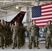 A formation of U.S. military personnel in OCP (Operational Camouflage Pattern) uniforms stand at parade rest inside a military hangar. Behind them is a large American flag and the tail section of a military aircraft bearing the markings 'AC 177FW' and 'New Jersey', identifying this as the 177th Fighter Wing of the New Jersey Air National Guard. The setting appears to be a formal military ceremony or briefing.