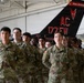 A group of U.S. Army soldiers in OCP (Operational Camouflage Pattern) uniforms stand at parade rest inside a military hangar. Behind them is the tail section of a black aircraft bearing the markings 'AC 177 FW' and 'New Jersey,' identifying it as belonging to the 177th Fighter Wing of the New Jersey Air National Guard. Two soldiers in the foreground are identifiable by name tapes: 'CARLOS' and 'PAEZ.'