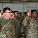 A group of U.S. Army soldiers are raising their right hands in what appears to be a re-enlistment or oath of enlistment ceremony. The soldiers are wearing Army Combat Uniforms (ACU) in Operational Camouflage Pattern (OCP). The ceremony is taking place indoors, likely in a military hangar or large facility.