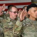 A group of U.S. Army soldiers are raising their right hands in what appears to be a military oath ceremony, likely a reenlistment or enlistment swearing-in. The soldiers are wearing OCP (Operational Camouflage Pattern) uniforms with name tapes visible, including 'RAUB' and 'ZAMORA'. An American flag is partially visible in the background, consistent with a formal military ceremony setting.