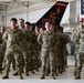 A formation of U.S. Army soldiers in MultiCam/OCP camouflage uniforms standing at parade rest inside a military hangar. Behind them is a fighter jet tail fin marked 'New Jersey AC 177 FW' (177th Fighter Wing) and a large American flag. The setting appears to be a formal military ceremony or briefing at what is likely Atlantic City Air National Guard Base.