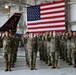 A group of military personnel in camouflage uniforms are raising their right hands in what appears to be a formal oath ceremony inside a military hangar. A large American flag is prominently displayed in the background, and a military aircraft tail fin bearing the markings '177 FW' and 'New Jersey' is visible, indicating this is likely at the 177th Fighter Wing of the New Jersey Air National Guard. The ceremony appears to be a reenlistment or enlistment swearing-in event.