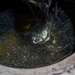 Cable specialists conduct maintenance hole inspection to support base operations