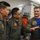 Three military personnel in olive/sage green flight suits are engaged in conversation inside what appears to be a military aircraft. Two individuals appear to be from an Asian air force (likely Thai, based on visible script and insignia), while the third on the right appears to be from a Western military, possibly the U.S. Air Force. The setting suggests a joint military exercise or liaison activity aboard a patrol or transport aircraft.