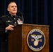 A U.S. Marine Corps officer in dress blues uniform is speaking at a podium at Marine Barracks Washington, D.C. The officer displays multiple medals and ribbons and appears to hold a general officer rank based on visible star insignia on the shoulders. The setting appears to be a formal military ceremony or official event.