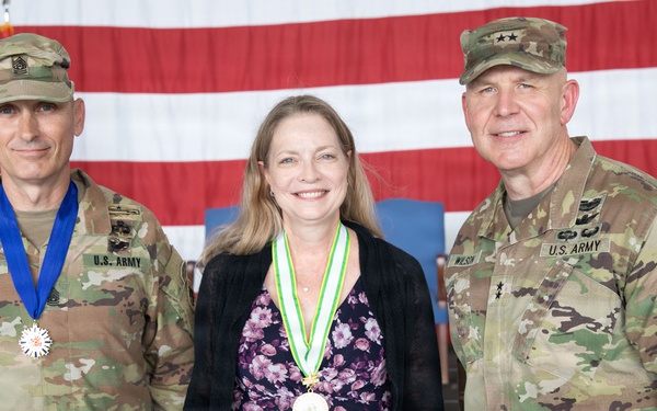 Three individuals pose for a formal photo at what appears to be a military awards ceremony. A civilian woman in the center holds a certificate from the State of Georgia Department of Defense for 'The Georgia Cherokee Rose Medal' and wears a green and white medallion. She is flanked by two U.S. Army soldiers in OCP (Operational Camouflage Pattern) uniforms, one of whom also wears a medal.