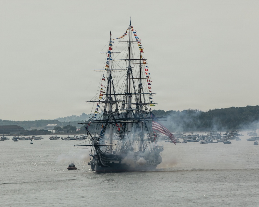 USS Constitution renders a gun salute during the Sail250 Boston Parade of Sail