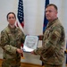 Two U.S. Air Force personnel in OCP (Operational Camouflage Pattern) uniforms are holding a Certificate of Promotion during a military promotion ceremony. The female officer on the left, identified by her name tape as 'FORSYTH' and wearing a Lieutenant Colonel oak leaf cluster, is presenting the certificate to the male recipient on the right, who wears a 'COMM' tab. The document appears to promote the recipient to Senior Master Sergeant.