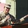 Medical Readiness Battalion welcomes new commander A female U.S. Army soldier in MultiCam (OCP) uniform is speaking at a podium while holding a microphone. She is gesturing with her right hand in an open-palm manner, suggesting she is delivering a speech or briefing. Behind her are military vehicles marked with red cross symbols, indicating a medical unit context.