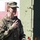 Medical Readiness Battalion welcomes new commander A U.S. Army soldier named Duimette is speaking into a microphone, likely addressing an audience at a military event. She is wearing Army Combat Uniform (ACU) in MultiCam pattern with visible unit patches including a 101st Airborne Division tab and a U.S. flag patch. A military medical vehicle with a Red Cross symbol is visible in the background.