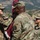 Medical Readiness Battalion welcomes new commander A U.S. Army ceremony is taking place outdoors, likely a change of command or unit activation event, with soldiers in OCP (Operational Camouflage Pattern) uniforms handling a maroon guidon or unit flag. The setting appears to be a military installation with mountains visible in the background, consistent with Fort Carson, Colorado. Multiple soldiers are participating, with one female soldier appearing to pin or adjust something on a male soldier's uniform.