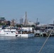 A U.S. Coast Guard vessel named 'Melvin Bell' (hull number 1105) is docked at a pier in what appears to be Boston Harbor, identifiable by the Leonard P. Zakim Bunker Hill Memorial Bridge visible in the background. The scene appears to be a public event or Fleet Week, as crowds of people are visible on the dock and along the waterfront. The image was taken from the water on a clear, sunny day.