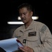 A U.S. Navy sailor in tan/khaki working uniform is reviewing documents in what appears to be a shipboard interior space. The individual's name tag reads 'SOTTO' and rank insignia indicates a Chief Petty Officer (HMC) with Surface Warfare and Fleet Marine Force qualifications. The setting is dimly lit with industrial overhead lighting visible in the background.