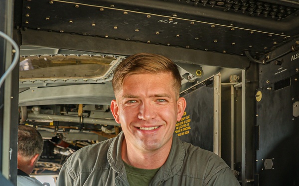 A U.S. Marine Corps Captain wearing an olive green flight suit stands smiling inside or at the entrance of a military aircraft. His name tag reads 'T.R. Runnels, CAPT, USMC' and he wears a squadron patch for VMM-165 'White Knights' along with naval aviator wings. The setting appears to be the interior of a tiltrotor or helicopter aircraft, likely an MV-22 Osprey given the squadron designation.