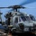 Routine Operations Aboard USS Mason (DDG 87) A U.S. Navy helicopter, numbered '707', is positioned on the flight deck of a naval vessel at sea with its rotors spinning. The aircraft appears to be an MH-60R Seahawk, identifiable by its distinctive nose-mounted sensors and gray naval paint scheme. The helicopter is chained to the deck and appears to be either preparing for takeoff or having just landed.