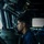 Routine Operations Aboard USS Mason (DDG 87) A young U.S. Navy sailor in a dark blue uniform is stationed at what appears to be a ship's bridge, looking through or operating a navigational instrument, likely a gyrocompass or bearing repeater. The setting is the interior of a naval vessel's pilothouse, filled with various electronic displays and control equipment. The image is dramatically lit with natural light coming through bridge windows.