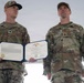 Two U.S. Coast Guard personnel in OCP (Operational Camouflage Pattern) uniforms stand at attention during a military awards ceremony. The individual on the left, identified by name tape as 'KRAUTLER,' holds an open certificate folder displaying a Meritorious Service Medal citation from the United States of America. The individual on the right, identified as 'PHILLIPS,' stands at parade rest beside him.