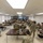 2026 Paralegal Warrior A large group of military personnel in camouflage uniforms (OCP/MultiCam pattern) are attending a briefing or training session in a classroom-style setting. The soldiers are seated at rows of tables facing a projection screen at the front of the room where a presenter is standing. The setting appears to be a military installation classroom or conference room.