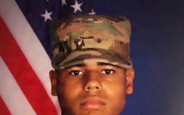 This is a formal U.S. Army military portrait photograph of a soldier identified by name tape as 'SWINTON'. The subject is wearing Operational Camouflage Pattern (OCP) uniform with a matching patrol cap, posed in front of an American flag and blue backdrop. This appears to be a standard military service portrait.