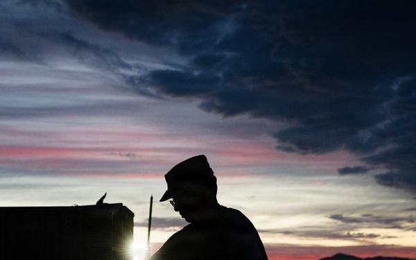 Soldier silhouetted against sunset sky during field operations