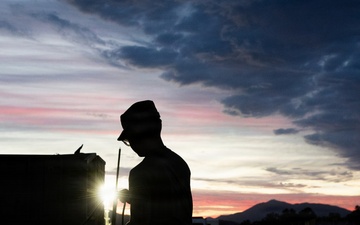 Soldier silhouetted against sunset sky during field operations