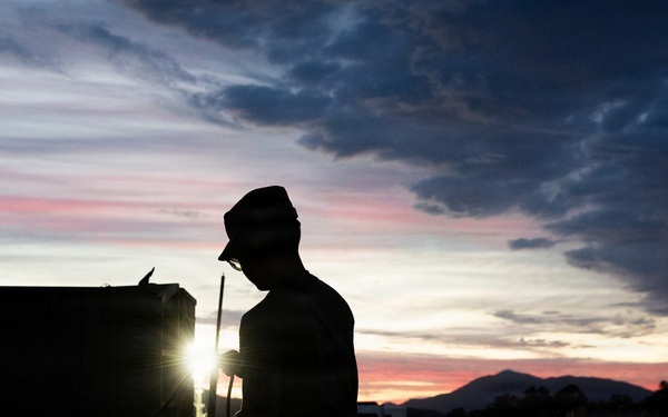 Soldier silhouetted against sunset sky during field operations
