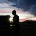 Soldier silhouetted against sunset sky during field operations