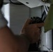 A person is working with their hands on what appears to be electrical or mechanical equipment in a confined space. They are holding a dark-colored tool or connector component and appear to be installing or adjusting it on an overhead panel or surface. The image is taken at close range with significant depth-of-field blur on the foreground elements.