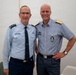Two senior military officers in light blue uniforms pose together for a photograph indoors. The officer on the left wears a US Air Force uniform with three-star rank insignia (Lieutenant General), while the officer on the right wears what appears to be a Scandinavian/Nordic air force uniform with two-star shoulder boards and a distinctive badge. Both are smiling in what appears to be an official or diplomatic meeting setting.
