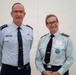 Two military officers in uniform are posing together for a photograph against a plain light-colored background. The officer on the left wears a US Air Force uniform with two-star (Major General) rank insignia and a name tag reading 'HEALY'. The officer on the right wears what appears to be a Royal Australian Air Force uniform with an Air Commodore rank insignia and a name badge/event tag.