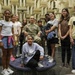 A group of approximately 11 children and young teenagers pose for a photo with a U.S. Army soldier in camouflage uniform who is seated in a chair. The group is gathered inside what appears to be an anechoic chamber, identifiable by the distinctive pyramid-shaped acoustic foam panels covering the walls. At least one student on the right is wearing a yellow 'GEMS' program t-shirt, suggesting this is an educational or STEM outreach visit.