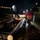 A nighttime flood rescue operation conducted by the West Virginia National Guard, showing personnel in red rescue suits and helmets standing in floodwater alongside an inflatable rescue boat. A large fallen tree log is visible in the foreground, partially blocking or resting against the rescue boat. The scene depicts an active flood emergency response in a residential area.