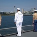 Four military personnel stand at the railing of a naval vessel looking toward a city skyline across the water. The Space Needle is clearly visible in the background, identifying the location as Seattle, Washington. The personnel are wearing a mix of U.S. Marine Corps and U.S. Navy dress uniforms, suggesting a formal occasion such as a fleet week or port arrival.