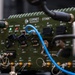 The image shows a military-grade electronic communications device manufactured by Cornet Technology, model STINN™, housed in an olive-drab green ruggedized enclosure. The unit features multiple labeled ports and connectors including Ethernet, USB, GPS, Wi-Fi, HDMI, and audio/radio interfaces. Several cables are actively connected to the device, including a visible blue Ethernet cable.