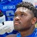 A close-up photograph of a male athlete wearing a blue Air Force football jersey, appearing fatigued or contemplative during what seems to be a game or practice session. His face shows visible sweat and exertion, and he is looking upward. A gloved hand holding a water bottle is visible in the foreground.