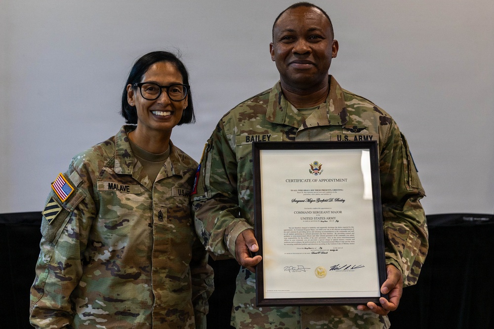 Two U.S. Army soldiers in OCP (Operational Camouflage Pattern) uniforms pose together for a photo. The soldier on the right, identified by name tape as 'BAILEY,' is holding a framed Certificate of Appointment designating him as Command Sergeant Major of the United States Army. The soldier on the left, identified as 'MALAVE,' appears to be presenting or celebrating the appointment with him.
