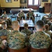 A group of military personnel in MARPAT (Marine digital camouflage) uniforms are seated in a circle in what appears to be a lounge or meeting room. Two senior personnel are seated centrally, appearing to lead or facilitate a discussion with the group. The setting suggests an informal briefing, mentorship session, or leadership engagement.