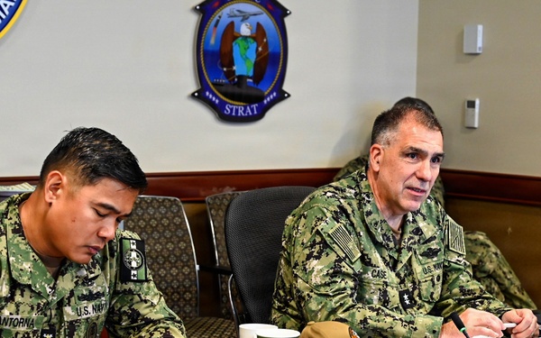 Two U.S. Navy personnel in digital camouflage uniforms (NWU Type III) are seated at a conference table during an official military meeting. The officer on the right, identified by his nameplate as 'Acting U.S. Navy Surgeon General' (name tag reads 'CASE'), appears to be speaking. The enlisted member on the left, identified as 'CANTORNA' with the title 'Force Master Chief BUMED,' is taking notes.