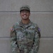 A U.S. Army soldier named Lara-Martinez is posing for a portrait in front of a stone wall. The soldier is wearing the standard Army Combat Uniform (ACU) in OCP (Operational Camouflage Pattern) and is smiling at the camera. The image appears to be an official or semi-official military portrait.