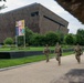 Military or National Guard personnel in camouflage uniforms are patrolling a walkway near the Smithsonian National Museum of African American History and Culture (NMAAHC) on the National Mall in Washington, D.C. A colorful Smithsonian banner reading '250' and 'Our Shared Future' is visible near the museum's distinctive bronze-latticed exterior. The scene suggests a period of heightened security presence at a major national institution.