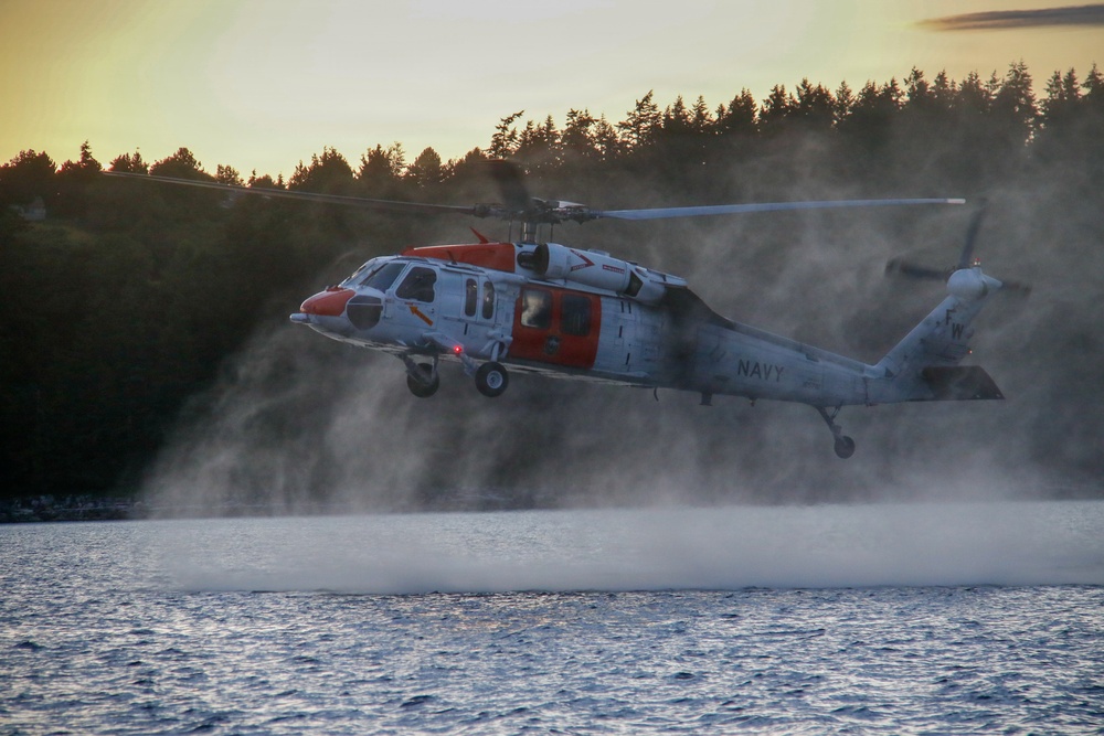 U.S. Navy MH-60S Seahawk helicopter performs low hover over water during training operations at sunset