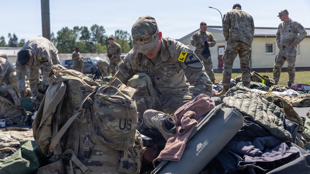 U.S. Army soldiers are conducting a gear inspection or layout drill in an outdoor area, likely on a military installation. Multiple soldiers in OCP (Operational Camouflage Pattern) uniforms are sorting through and organizing large amounts of military equipment spread across the ground. The scene appears to be a formal equipment accountability or pre-deployment inspection.