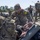 USAREUR-AF Best Squad Competition Day Zero Layout U.S. Army soldiers are conducting a gear inspection or layout drill in an outdoor area, likely on a military installation. Multiple soldiers in OCP (Operational Camouflage Pattern) uniforms are sorting through and organizing large amounts of military equipment spread across the ground. The scene appears to be a formal equipment accountability or pre-deployment inspection.